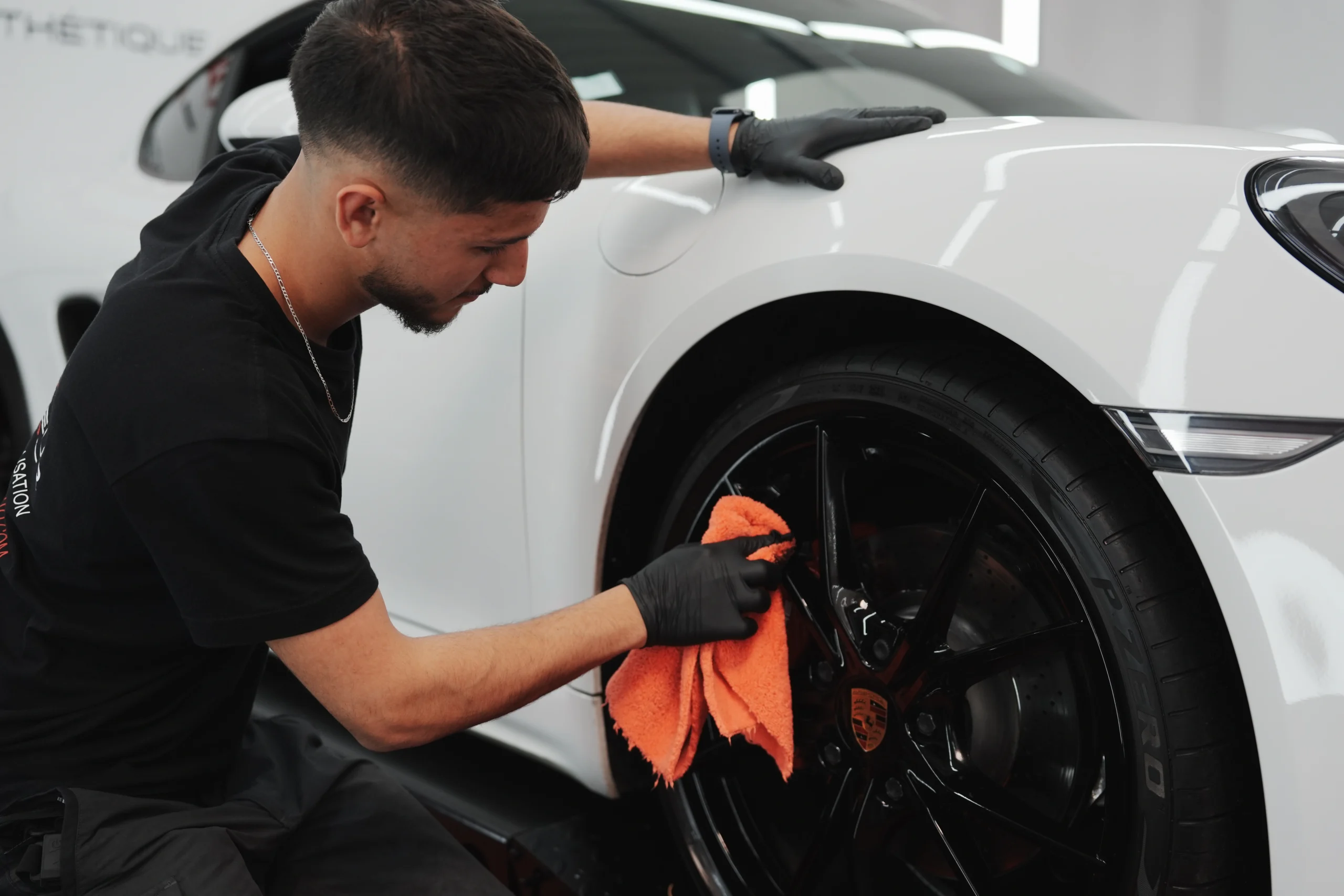 Technicien Fraicheur Auto nettoyant à la microfibre la jante d'une Porsche blanche en atelier