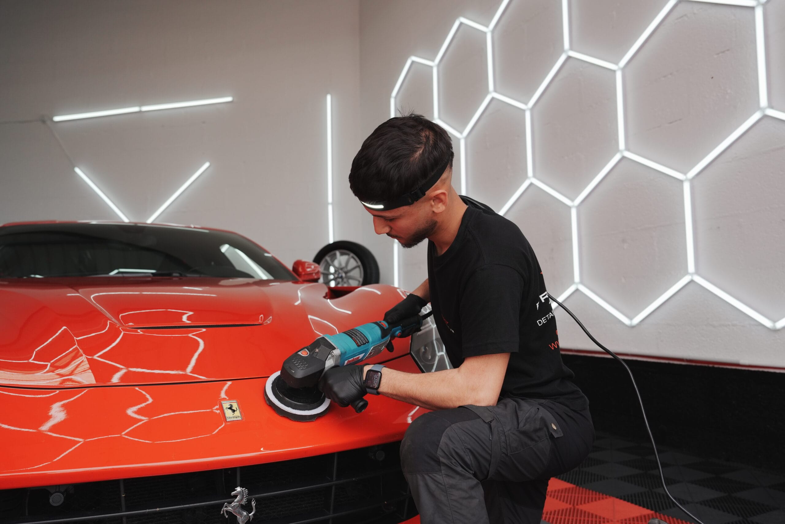 Abulfaz polissant la carrosserie d'une Ferrari rouge à la polisseuse en atelier à Sautron
